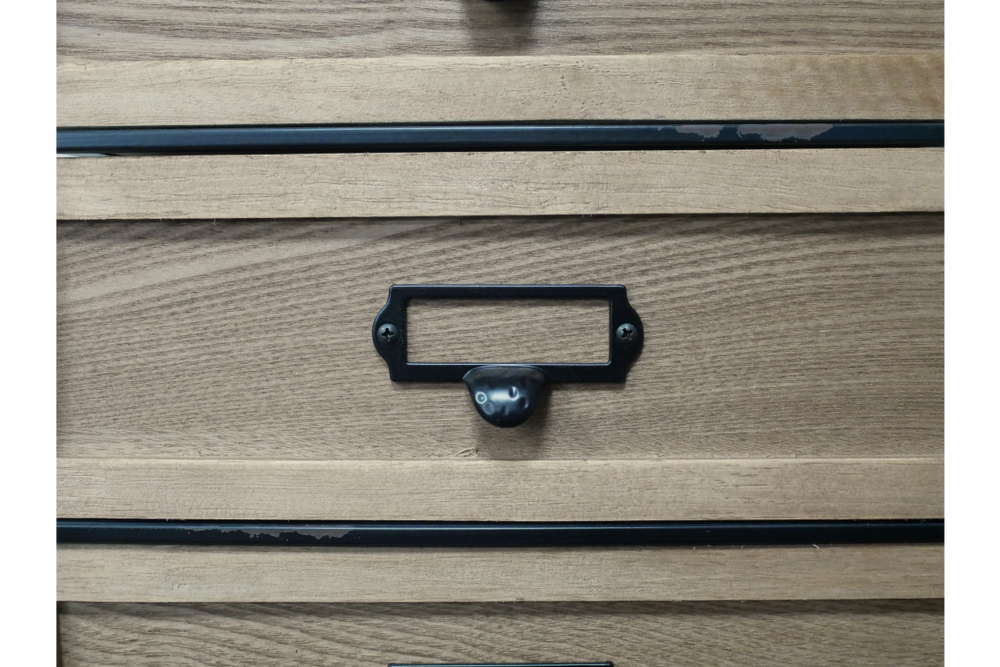 Close-up of light brown wooden industrial drawer cabinet with black metal handle and label holder.