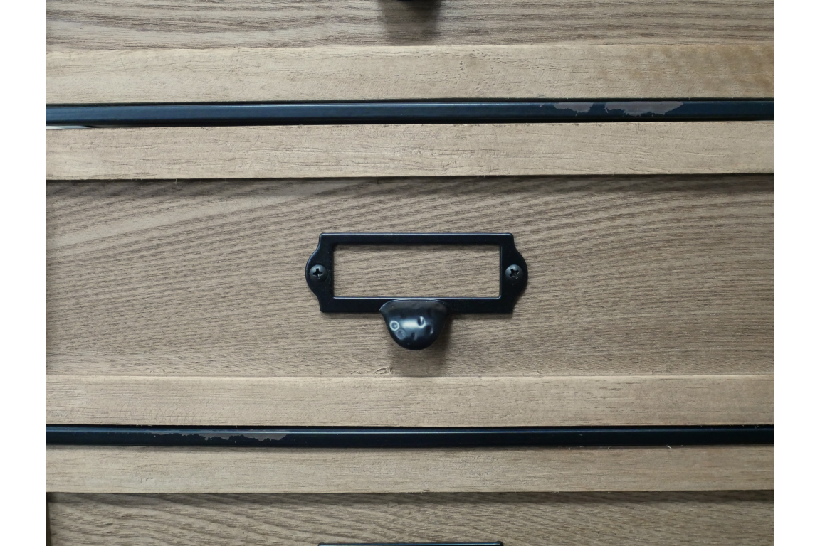 Close-up of light brown wooden industrial drawer cabinet with black metal handle and label holder.