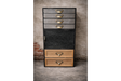 Tall industrial drawer cabinet with mixed metal and wood drawers, black frame, brass handles, front view against textured