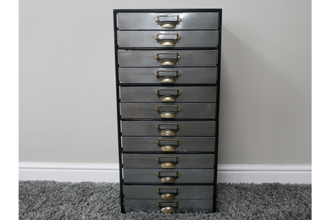 Tall industrial drawer cabinet with ten metal drawers and brass handles, front view on gray carpet.