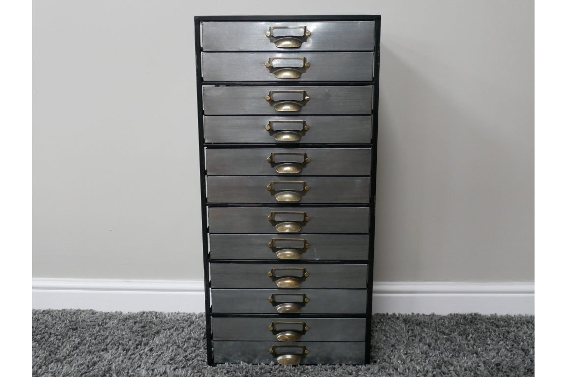 Tall industrial drawer cabinet with ten metal drawers and brass handles, front view on gray carpet.