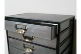 Metal industrial drawer cabinet with five drawers, brass handles, shown from front angle with one drawer open.