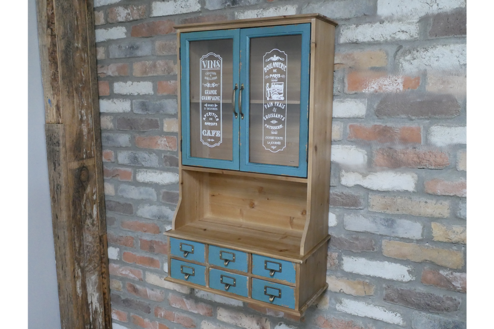 Wooden Parisienne wall unit with blue cabinet doors and six blue drawers, against a rustic brick wall, angled view.