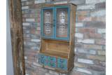 Wooden Parisienne wall unit with blue cabinet doors and six blue drawers, against a rustic brick wall, angled view.