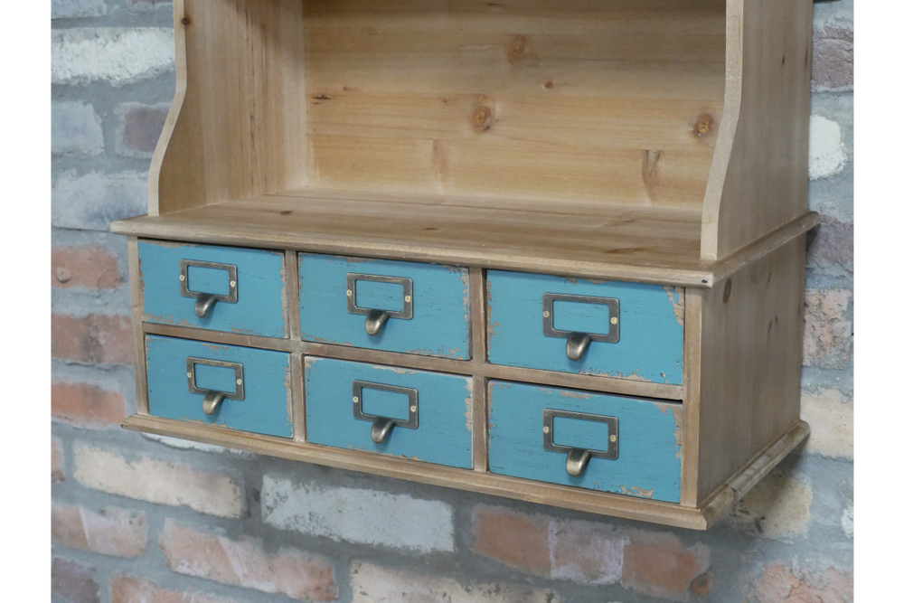 Wooden wall unit with six distressed blue drawers and metal handles, shown at an angle against a brick wall.