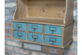 Wooden wall unit with six distressed blue drawers and metal handles, shown at an angle against a brick wall.
