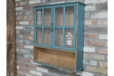 Blue wooden wall unit with two glass paneled doors and open shelf below, mounted on a brick wall, side angle view.