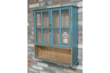 Blue wooden Parisienne Wall Unit with glass paneled doors and open lower shelf, mounted on brick wall.