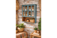 Wall-mounted wooden kitchen unit in distressed blue with glass paneled doors, displayed at an angle against a brick wall.