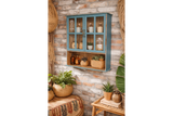 Wall-mounted wooden kitchen unit in distressed blue with glass paneled doors, displayed at an angle against a brick wall.