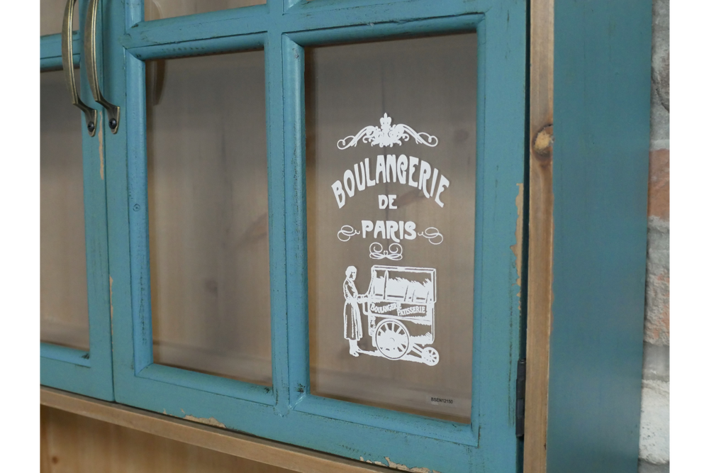 Close-up of distressed blue wooden wall unit with glass pane door featuring vintage white bakery illustration and text.