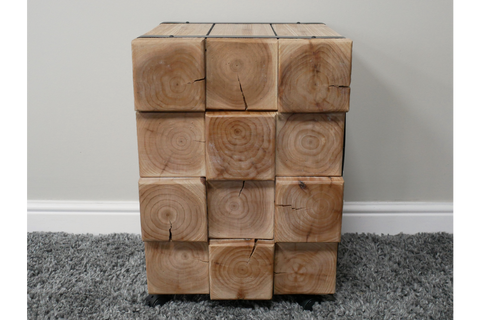 Chunky bedside cabinet made of natural wood blocks with visible grain and cracks, front view on carpeted floor.