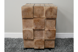 Chunky bedside cabinet made of natural wood blocks with visible grain and cracks, front view on carpeted floor.