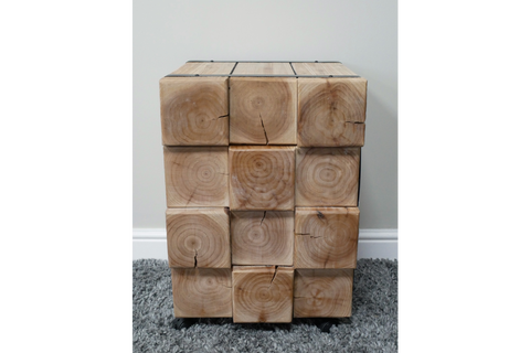 Chunky bedside cabinet made of natural wood blocks showing grain and cracks, front view on gray carpet.