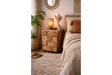 Chunky bedside cabinet made of natural wood blocks with visible rings, shown at a bedroom corner with decorative items on