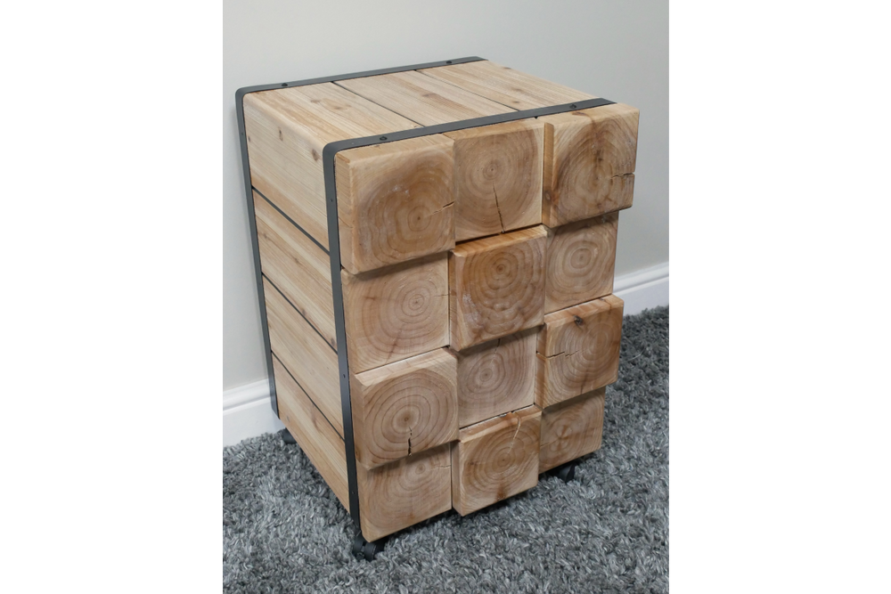 Chunky bedside cabinet made of light natural wood blocks with visible grain, metal frame, and caster wheels, shown at an