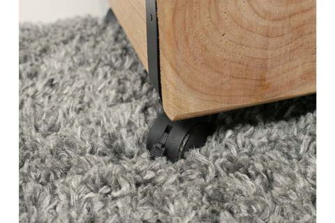 Close-up of light wood chunky bedside cabinet corner with black caster wheel on gray shag carpet