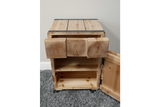 Light wood chunky bedside cabinet with open drawer and door showing interior shelving, placed on gray carpet.