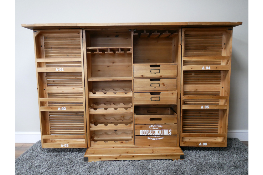 Wooden shutter bar cabinet with open doors, multiple shelves, drawers, and wine racks, front view on grey carpet.