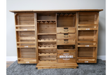 Wooden shutter bar cabinet with open doors, multiple shelves, drawers, and wine racks, front view on grey carpet.