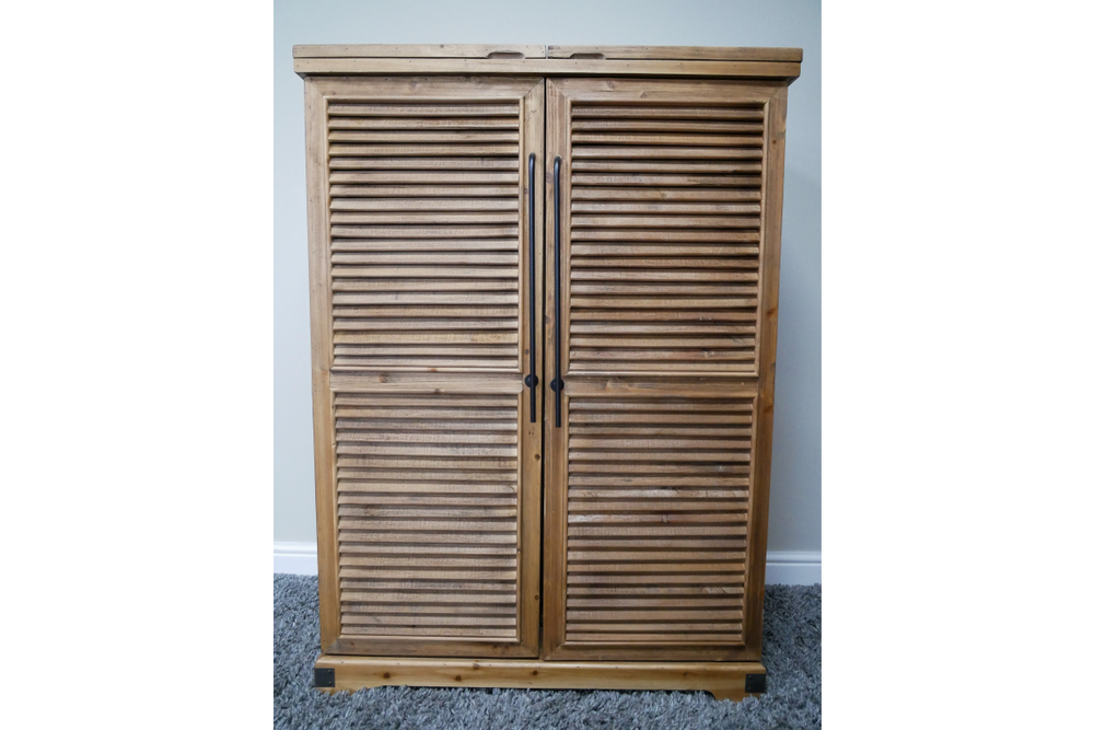 Wooden shutter style bar cabinet with two doors and black vertical handles, photographed front view on carpeted floor.
