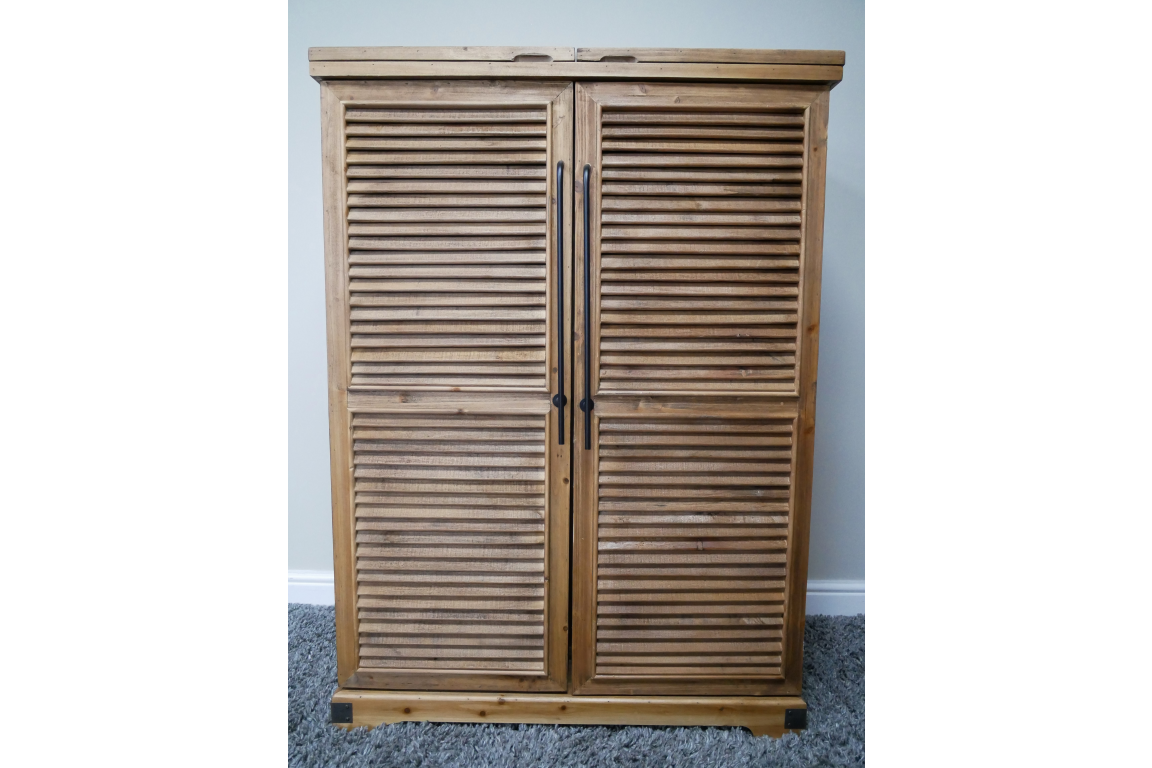 Wooden shutter style bar cabinet with two doors and black vertical handles, photographed front view on carpeted floor.