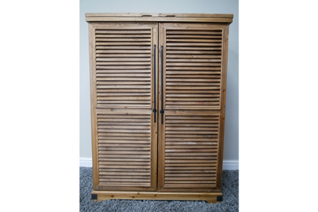 Wooden shutter style bar cabinet with two doors and black vertical handles, photographed front view on carpeted floor.