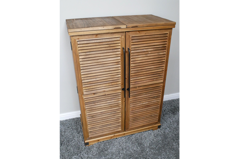 Wooden shutter bar cabinet with two doors, black handles, standing on grey carpet against a white wall.