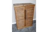 Wooden shutter bar cabinet with two doors, black handles, standing on grey carpet against a white wall.