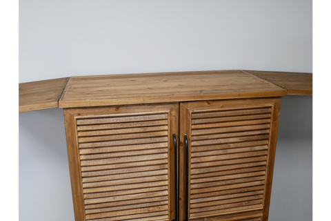 Wooden shutter bar cabinet with fold-out wing doors, black handles, photographed from front angle against white wall.