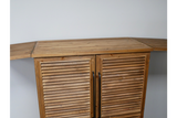 Wooden shutter bar cabinet with fold-out wing doors, black handles, photographed from front angle against white wall.
