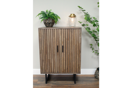 Wooden 2 door slatted cabinet in natural finish with black handles and legs, shown from front in indoor setting.