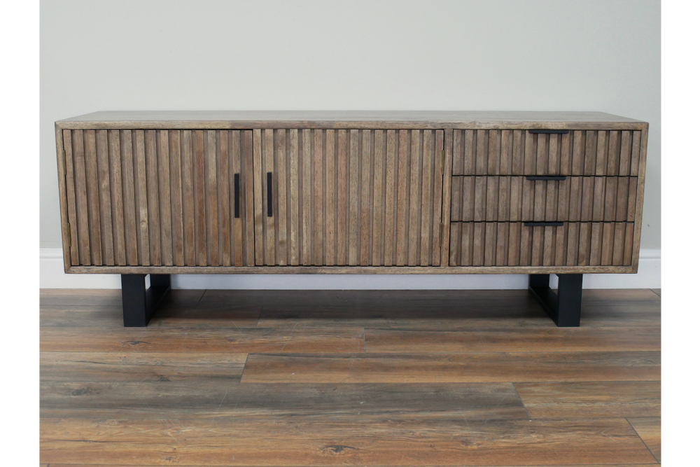 Low wooden slatted TV sideboard with black metal legs, two doors and three drawers, front view on wooden floor.