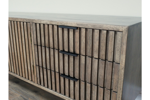 Wooden TV low sideboard with slatted door and drawers, black handles, angled view on light-colored floor.