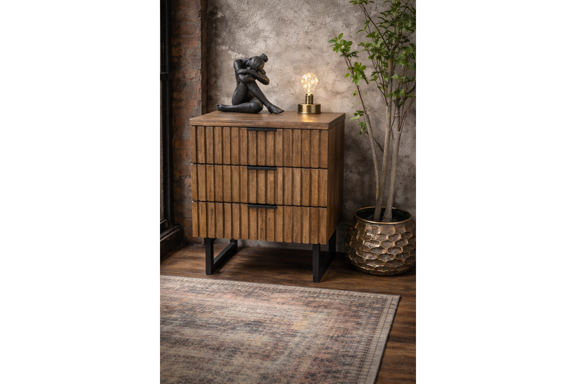 Wooden slatted bedside cabinet with three drawers and black metal legs, shown at an angle in a rustic room setting.
