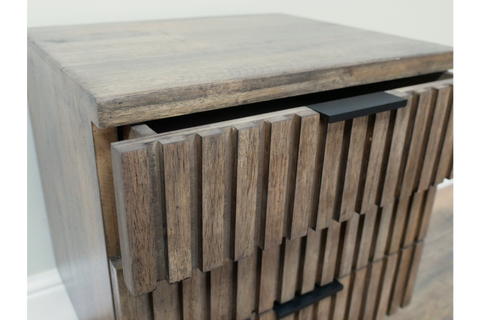 Slatted bedside cabinet in natural wood finish with two drawers, angled view showing texture and black handles.