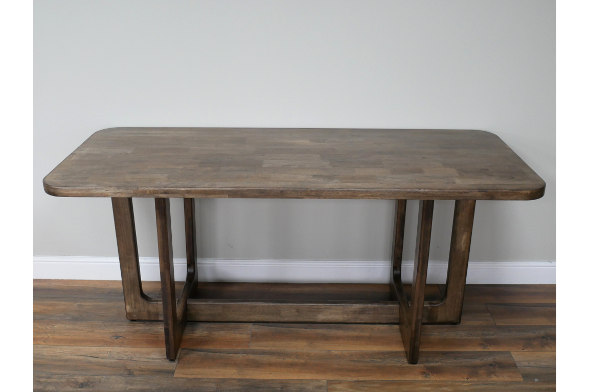 Rectangular wooden dining table with rounded corners, visible wood grain, and geometric leg design, front view.
