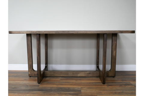 Rectangular dining table with dark wooden top and sturdy legs, shown from the front against a plain wall.