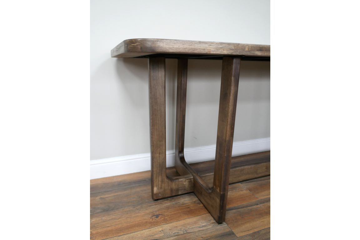 Wooden dining table with rectangular top and sturdy square legs, angled close-up view on wooden floor.