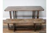 Rectangular wooden dining table with matching bench, natural brown finish, front angle on wooden floor.