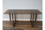 Rectangular dining table with a tinted glass top and wooden trestle legs, shown from front angle on wooden floor.