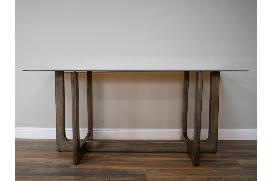 Rectangular dining table with clear glass top and dark wooden U-shaped legs, front view on wooden floor.