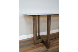 Dining table with clear glass top and wooden legs, side angle view on wooden floor against white wall.