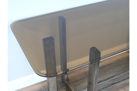 Rectangular dining table with tinted glass top and wooden legs, shown from a top corner angle.