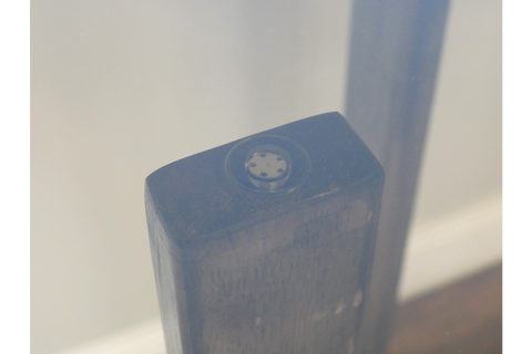 Close-up detail of dark wooden leg with black adjustable foot under clear glass tabletop viewed at an angle.