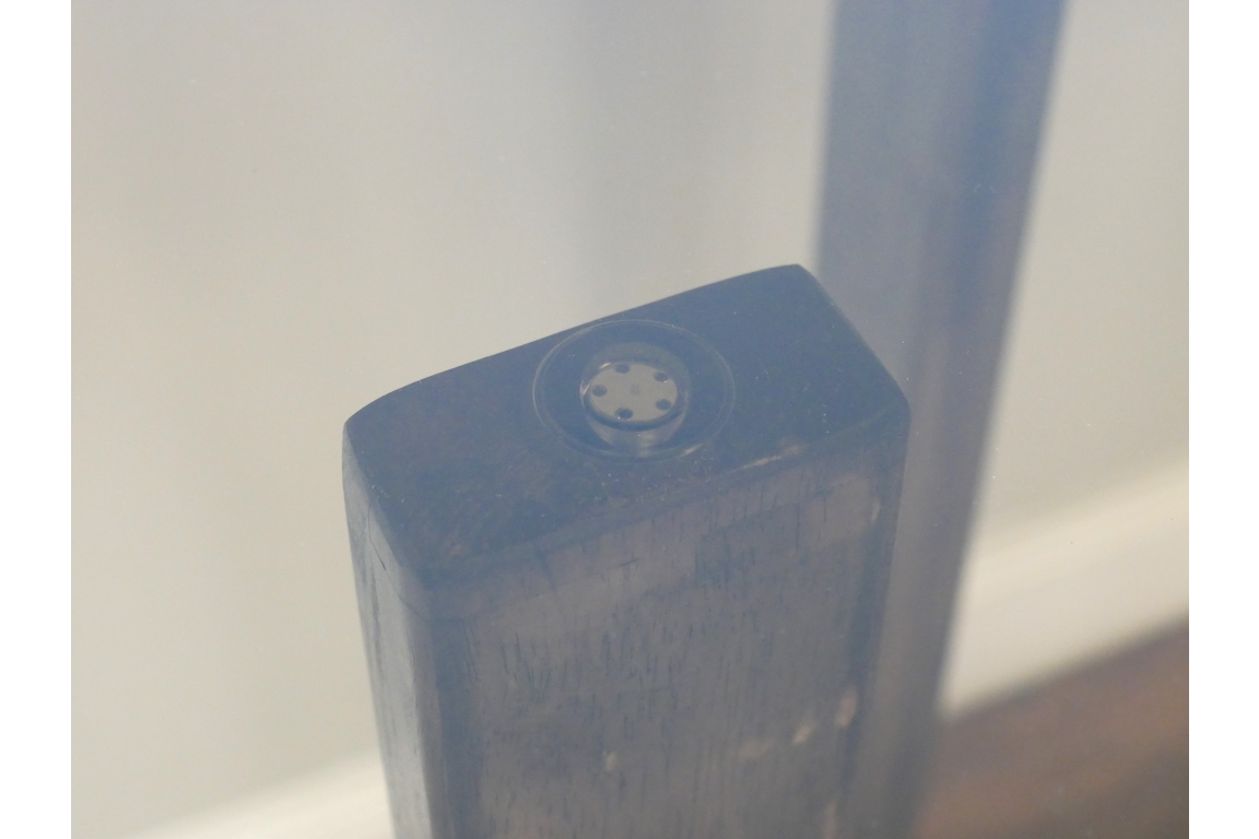 Close-up detail of dark wooden leg with black adjustable foot under clear glass tabletop viewed at an angle.