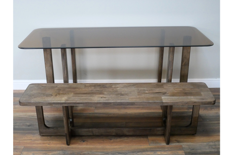 Rectangular dining table with smoky glass top and rustic brown wooden base, shown front view on wooden floor.