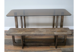 Rectangular dining table with smoky glass top and rustic brown wooden base, shown front view on wooden floor.