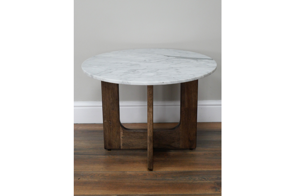 Round marble top side table with dark wood base, front view on wooden floor and light gray wall background.