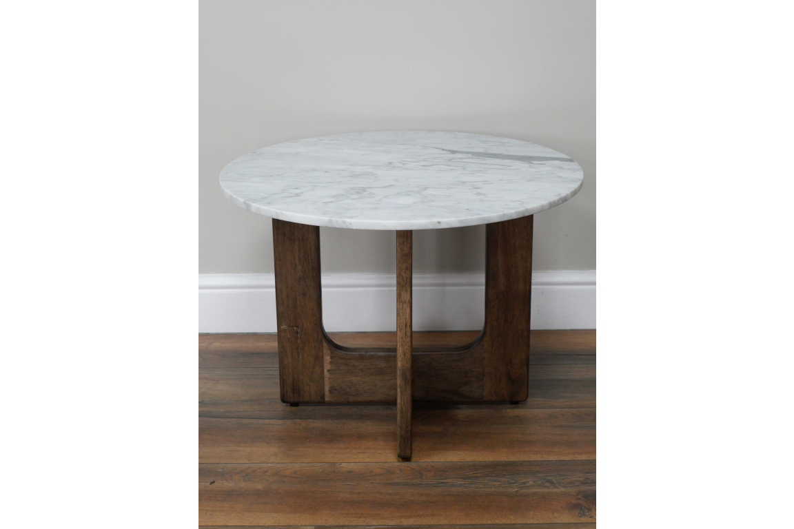 Round marble top side table with dark wood base, front view on wooden floor and light gray wall background.